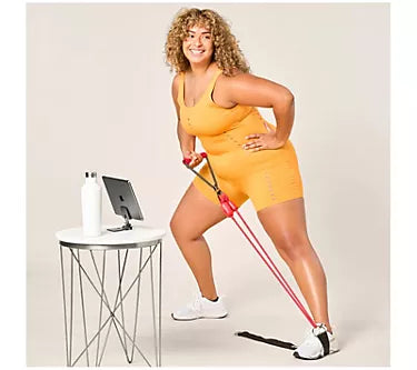 Woman in yellow athletic wear using resistance bands in a home setting.